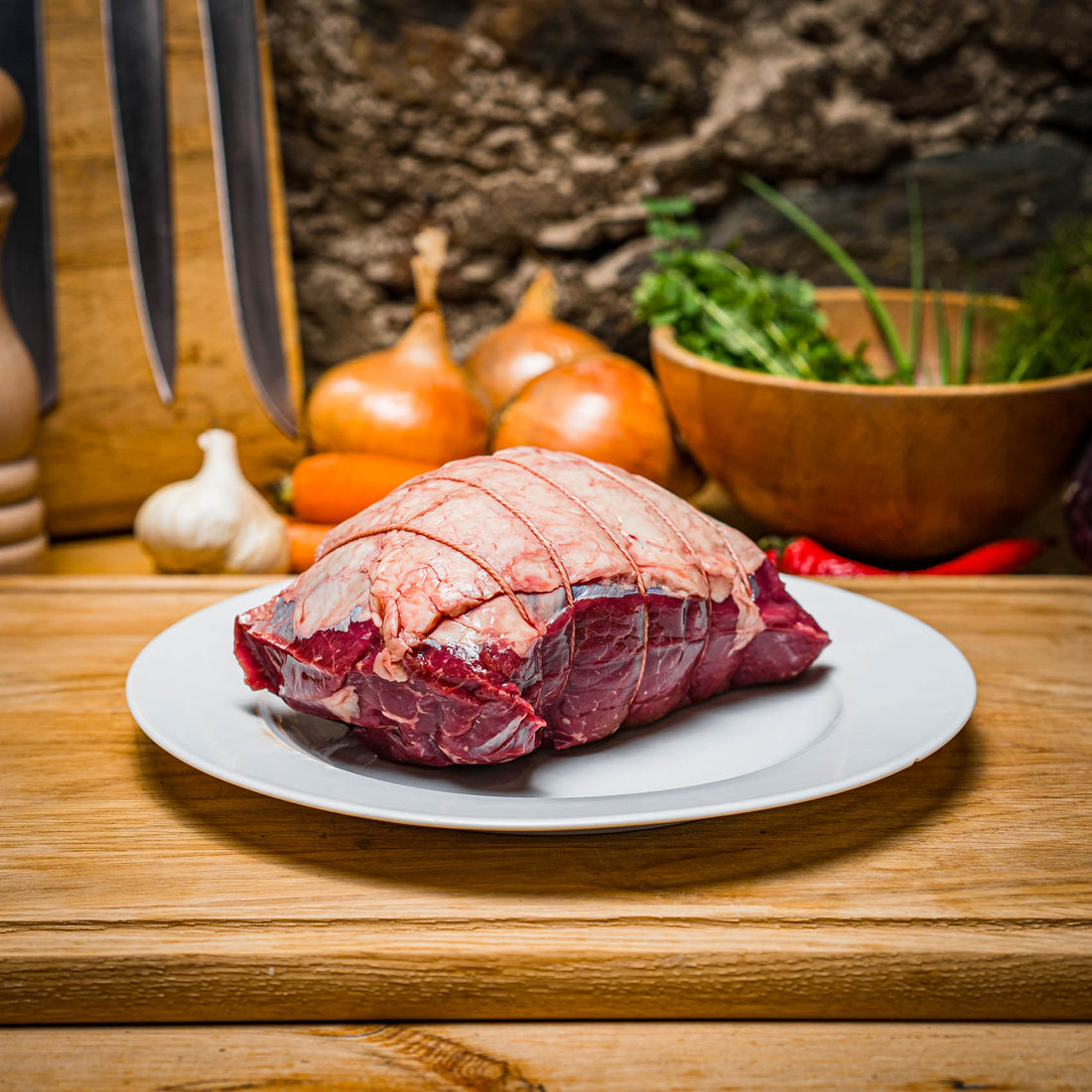 organic beef topside on a plate. chopping board and other ingredients for a delicious roast in the background